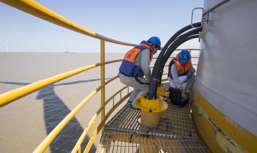 Technicians in safety gear performing maintenance on an offshore wind turbine.