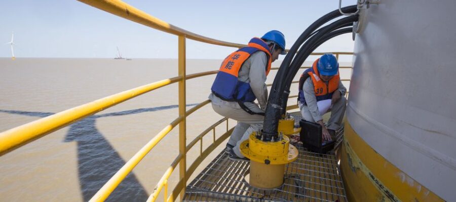 Technicians in safety gear performing maintenance on an offshore wind turbine.