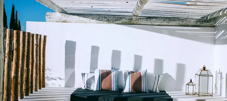 Textile with soft cushions near wall with shades under rough roof on veranda in sunlight