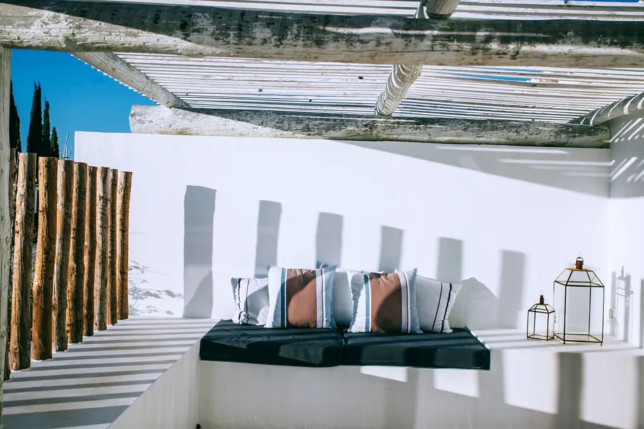 Textile with soft cushions near wall with shades under rough roof on veranda in sunlight