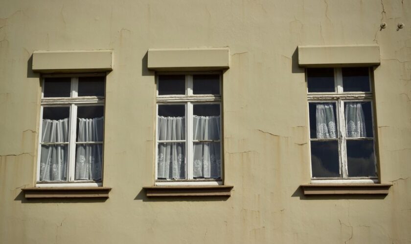 Three vintage windows with white curtains on a beige wall, capturing architectural charm.