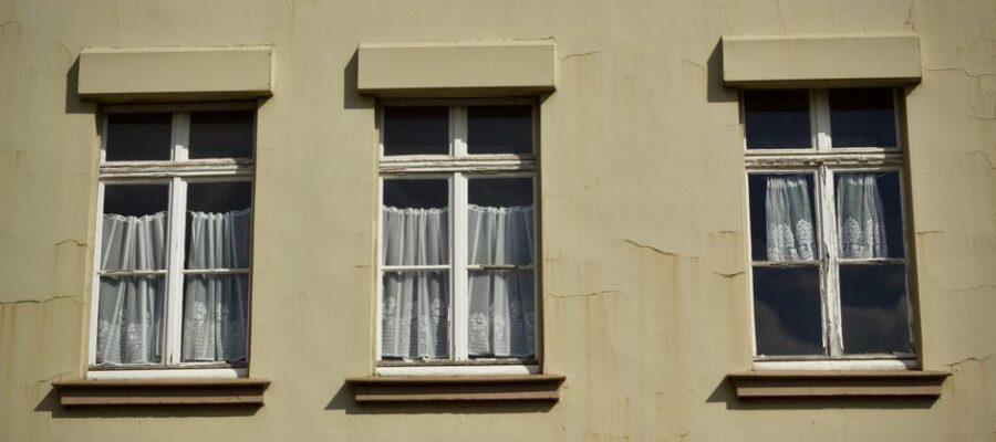 Three vintage windows with white curtains on a beige wall, capturing architectural charm.
