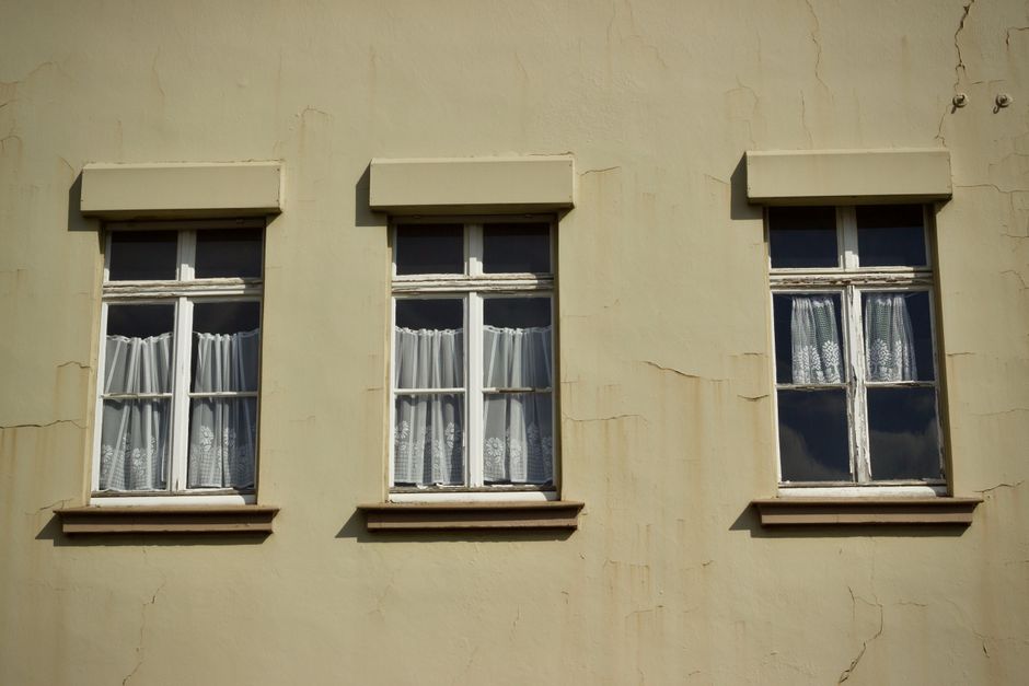 Three vintage windows with white curtains on a beige wall, capturing architectural charm.