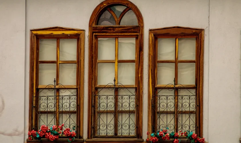 Three wooden windows with vibrant flower boxes on a vintage facade.