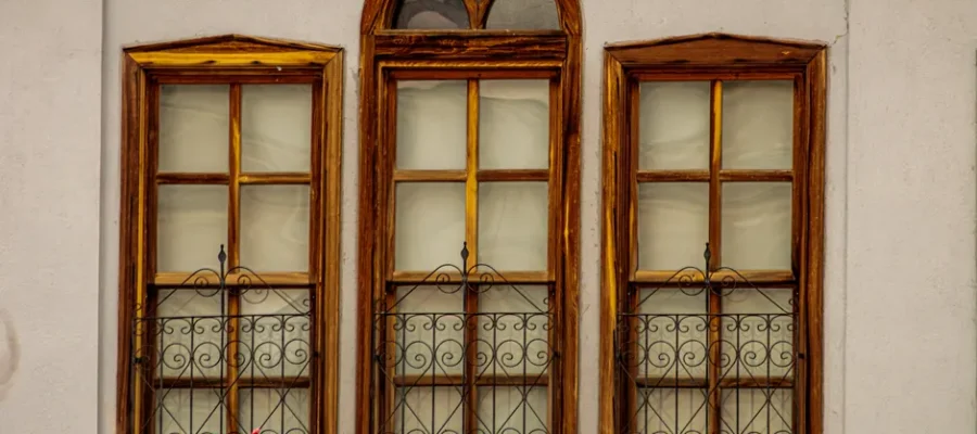 Three wooden windows with vibrant flower boxes on a vintage facade.