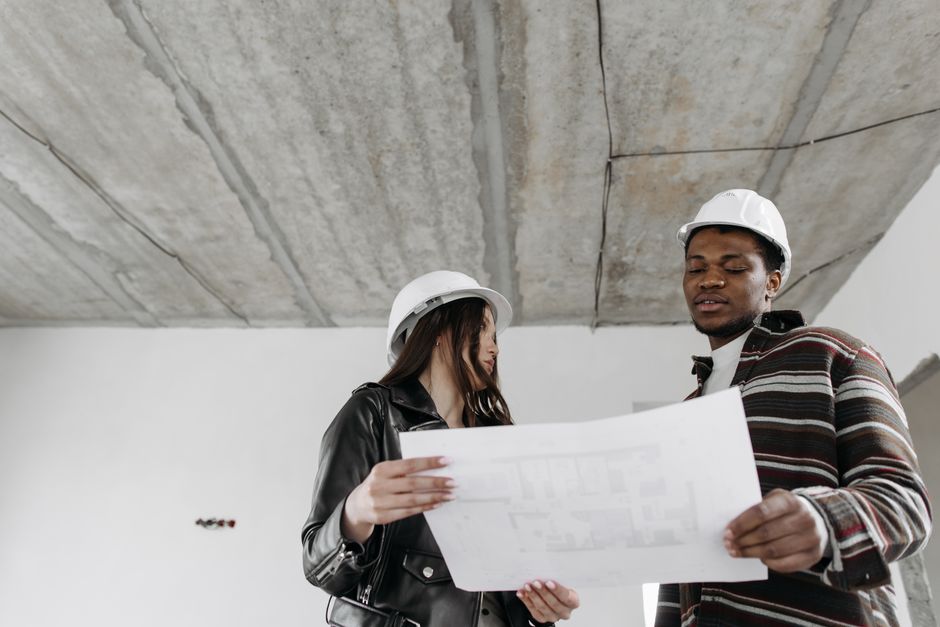 Two architects in hard hats examining blueprints in an unfinished building.