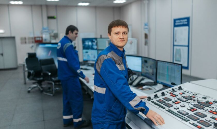 Two technicians operating machinery in a modern control room. Industrial setting with advanced equipment.