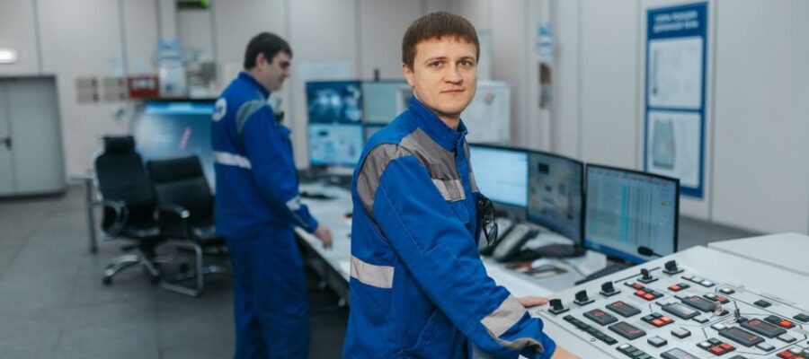 Two technicians operating machinery in a modern control room. Industrial setting with advanced equipment.