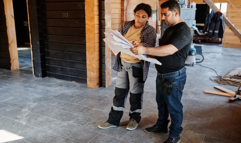 Two workers examining blueprints inside a building under construction, showcasing teamwork.
