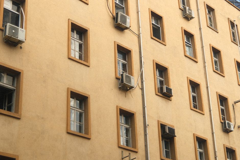 Urban building wall with air conditioners and windows on a sunny day.
