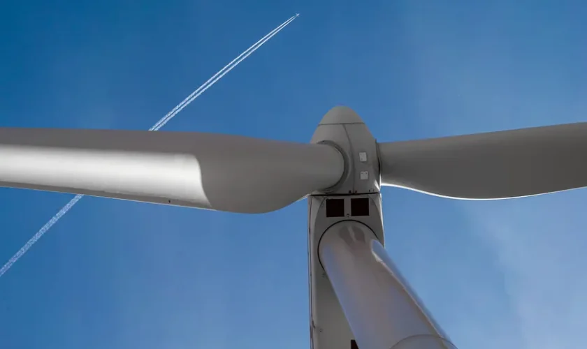 View of a wind turbine with a clear blue sky and airplane contrail in Ciudad Real, Spain.