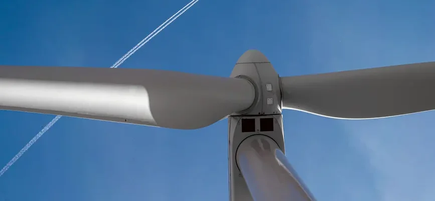View of a wind turbine with a clear blue sky and airplane contrail in Ciudad Real, Spain.