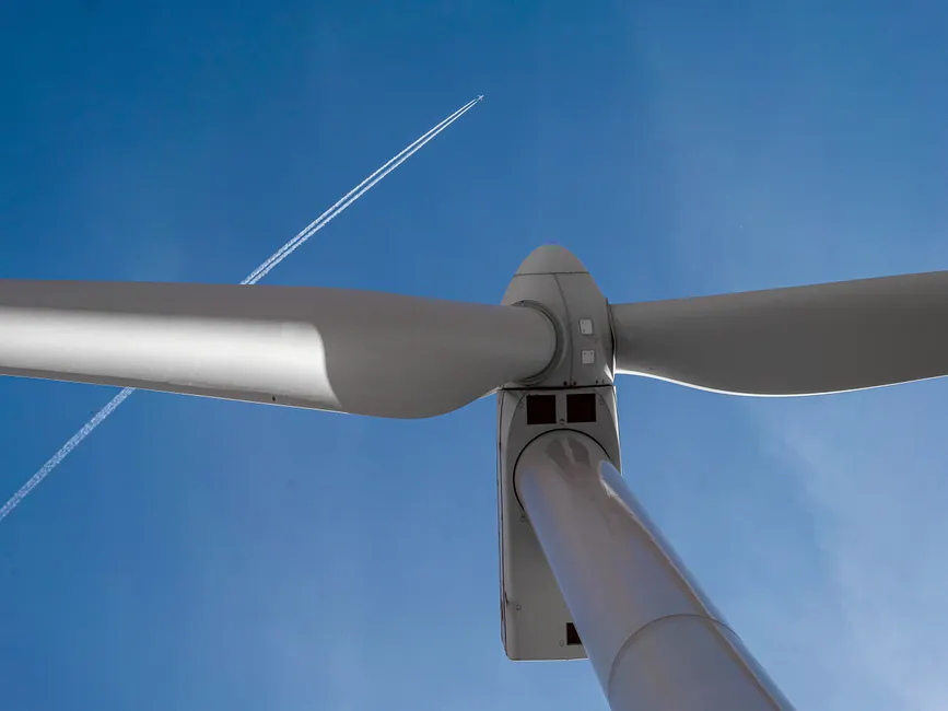 View of a wind turbine with a clear blue sky and airplane contrail in Ciudad Real, Spain.