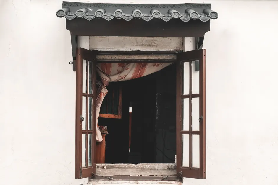 View of an open window with a wooden frame and curtain in a traditional setting.