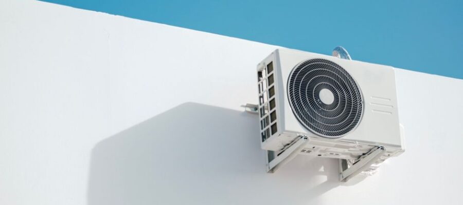 Wall-mounted air conditioner unit on a white building, set against a clear blue sky, creating a minimalist aesthetic.
