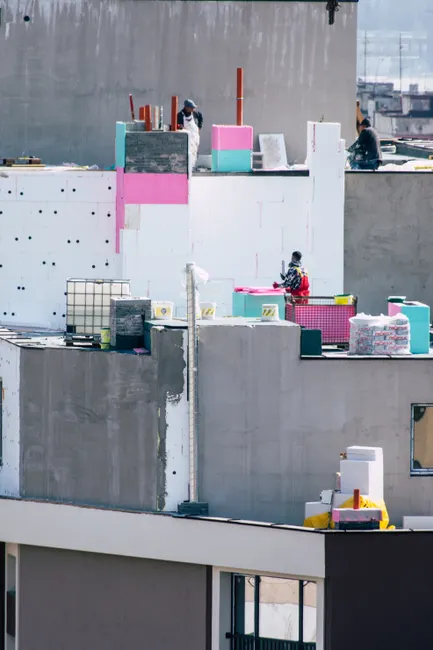 Workers on a city rooftop in bright daylight, engaged in construction activities with colorful insulation materials.