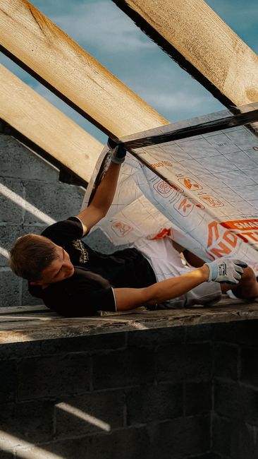 Young construction worker installing insulation on a roof during daylight. Captured outdoors with natural lighting.
