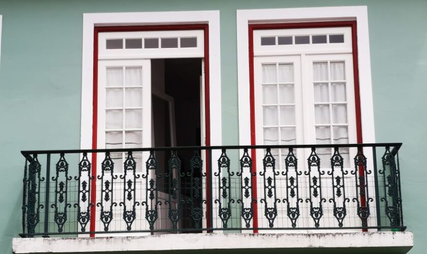 A beautifully designed balcony with ornate ironwork and white French doors on a green facade.