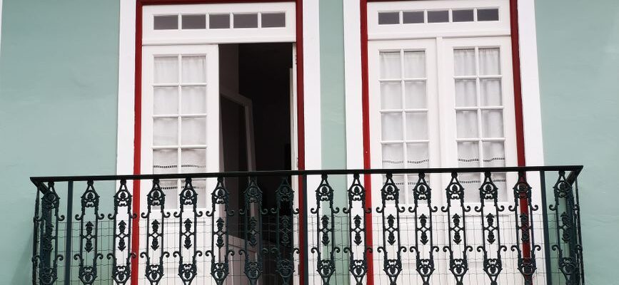 A beautifully designed balcony with ornate ironwork and white French doors on a green facade.