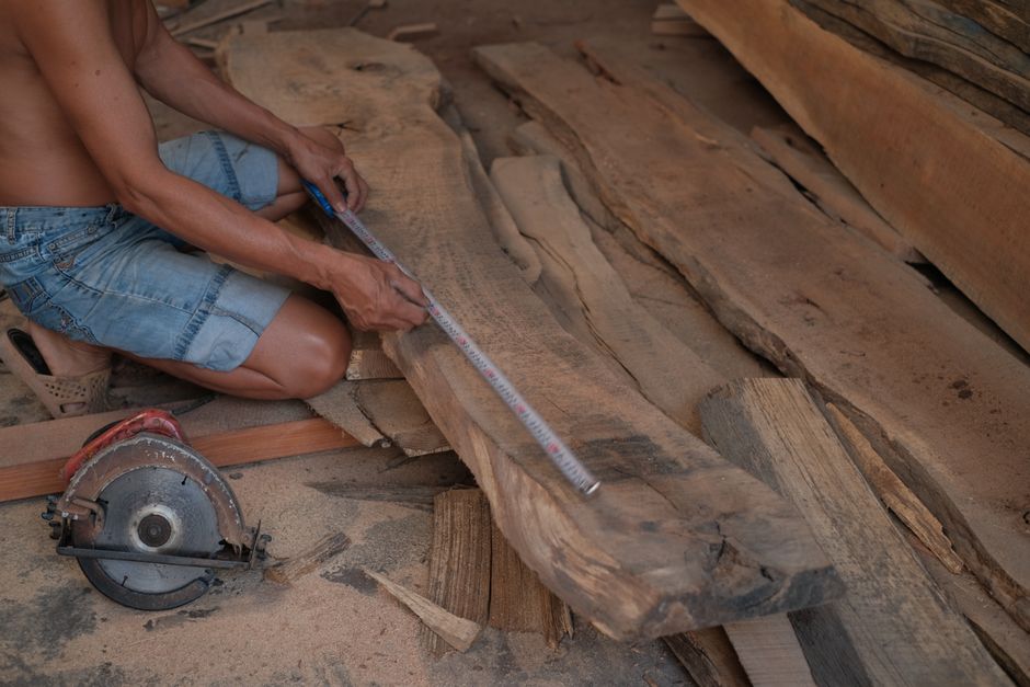 A carpenter precisely measuring a wooden plank, preparing for woodworking projects.