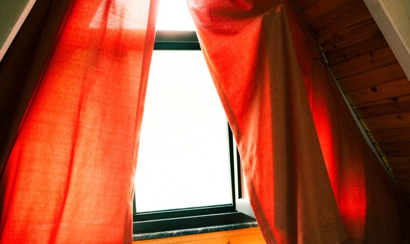 A cozy attic window with red curtains letting in warm sunlight, creating a serene indoor atmosphere.