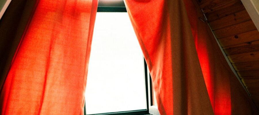 A cozy attic window with red curtains letting in warm sunlight, creating a serene indoor atmosphere.