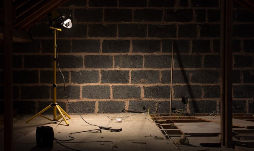 A dimly lit attic space under renovation with a construction lamp illuminating the scene.
