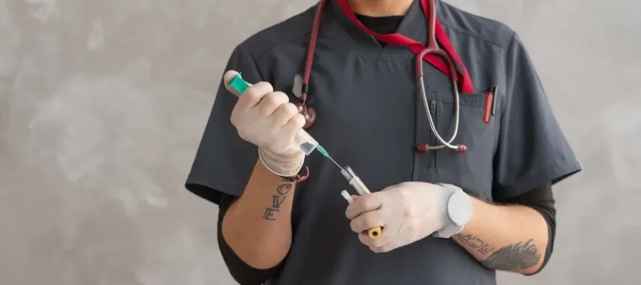 A healthcare worker in scrubs prepares a syringe with precision.