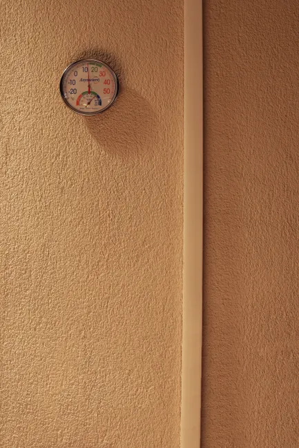 A minimalist indoor scene featuring a hygrometer mounted on a textured wall, indicating temperature and humidity.
