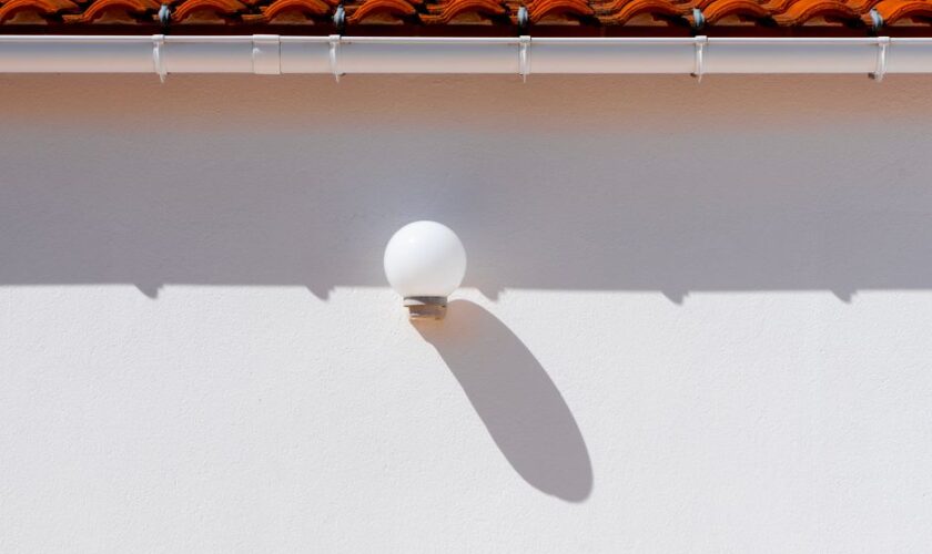A minimalist outdoor setting showcasing a wall lamp casting a shadow beneath a red tiled roof.