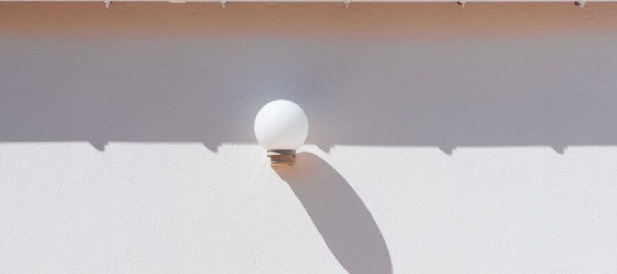 A minimalist outdoor setting showcasing a wall lamp casting a shadow beneath a red tiled roof.