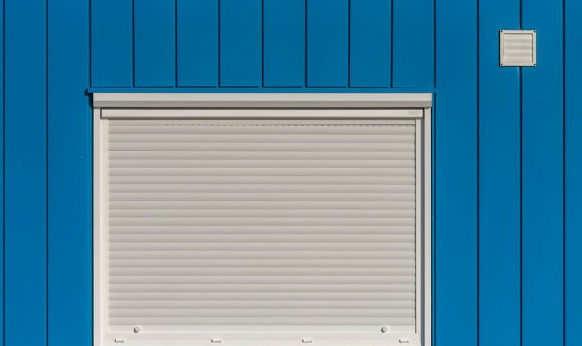 A modern blue wall with a closed white roller shutter, perfect for architectural designs.