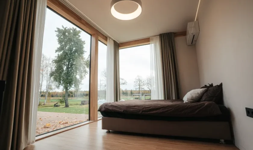 A modern minimalist bedroom with large windows overlooking a serene countryside landscape.