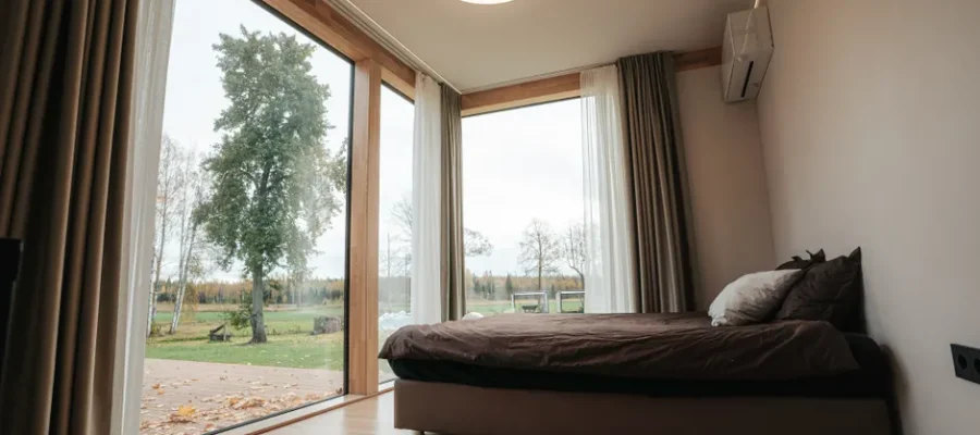 A modern minimalist bedroom with large windows overlooking a serene countryside landscape.
