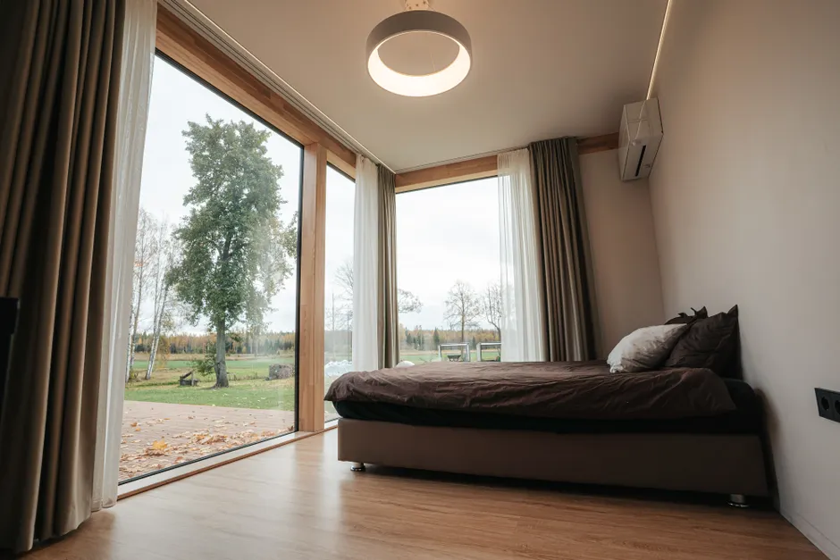 A modern minimalist bedroom with large windows overlooking a serene countryside landscape.