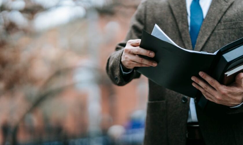 A professional in formal wear reviewing documents outside, showcasing business attire and focus.