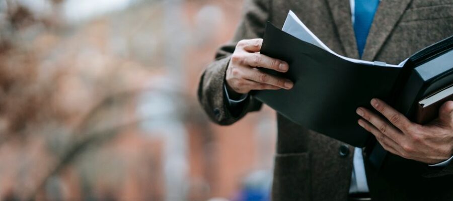 A professional in formal wear reviewing documents outside, showcasing business attire and focus.