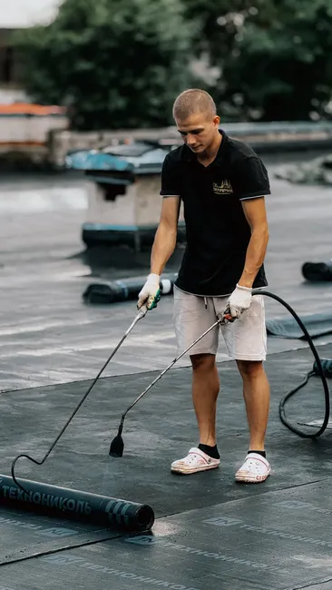 A roofer applies a waterproof membrane using a heat gun on a flat rooftop.