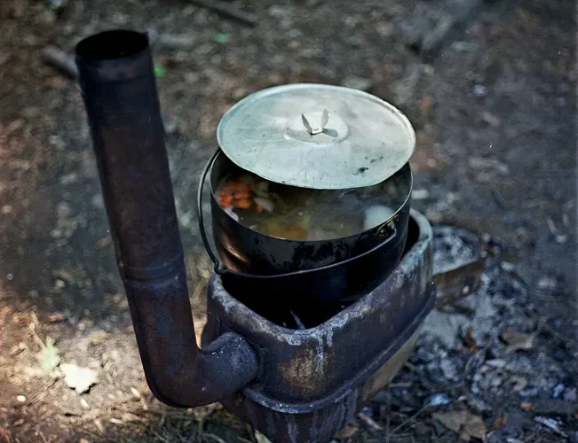 A rustic wood stove with a pot of food outdoors in a natural setting.