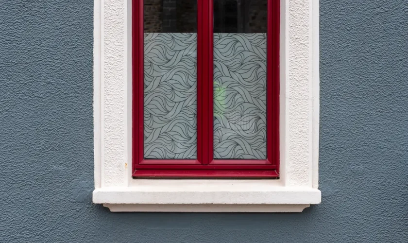 A stylish red-framed window with frosted glass against a textured blue wall.