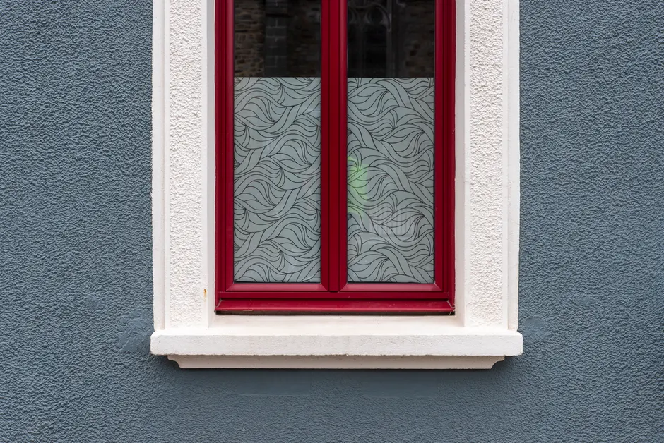 A stylish red-framed window with frosted glass against a textured blue wall.