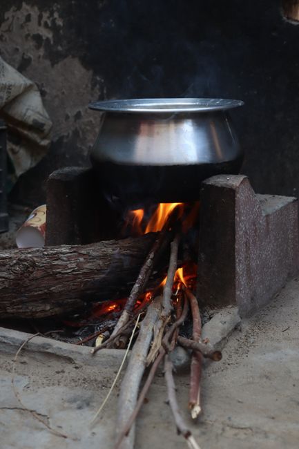 A traditional stove with a metal pot over an open fire fueled by wood logs outdoors.