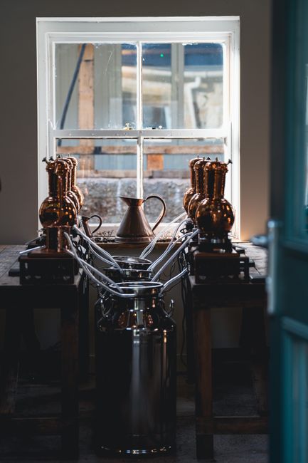 A vintage brewery setup featuring copper distillation equipment by a window.