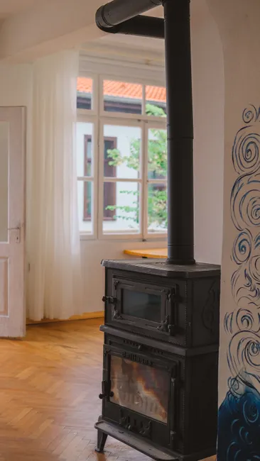 A vintage metal fireplace in a spacious, elegant home interior with wooden floors and large windows.