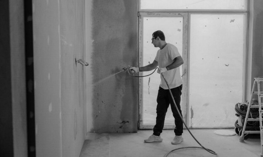 A worker paints an interior wall with a spray gun during a renovation project.