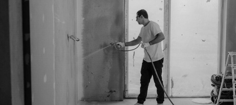 A worker paints an interior wall with a spray gun during a renovation project.