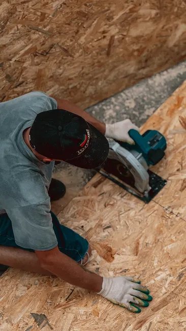 A worker using a circular saw to cut plywood during construction or renovation work.