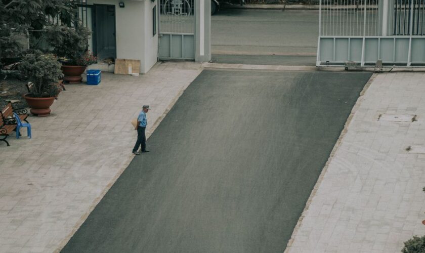 Aerial view of a man walking on a paved driveway lined with potted plants and a gate.