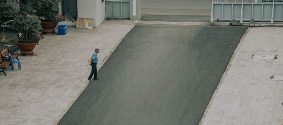 Aerial view of a man walking on a paved driveway lined with potted plants and a gate.