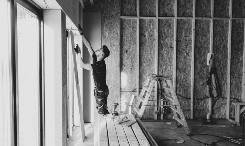 Black and white photo of a worker installing drywall indoors, Falun, Sweden.